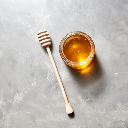 Sweet flower natural honey in a jar and wooden spoon on a gray concrete table, copy space. Top view. Jewish rosh hashanah holiday concept. Traditional useful sweetness.