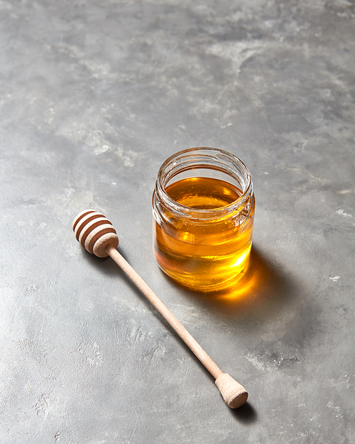Sweet flower natural honey in a jar and wooden spoon on a gray concrete table, place for text . Rosh hashanah jewish New Year holiday concept.