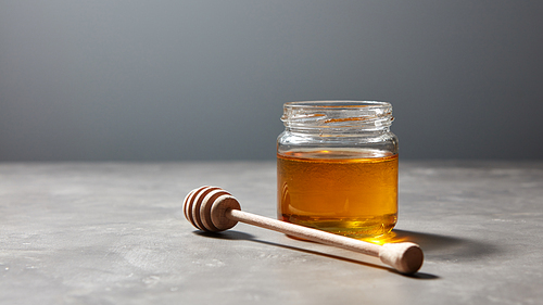 Aromatic fresh natural honey with dipper in a glass pot on a gray stone background, place under text. Rosh hashanah jewish concept. Traditional healthy swetnees.