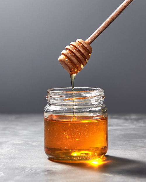 Dripping organic natural fresh honey from glass pot on a gray kitchen stone background with copy space. Jewish rosh hashanah holiday concept.