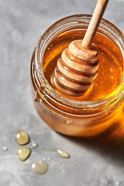 Wooden stick in a glass jar with aromatic natural organic honey on a gray marble table, place for text. Rosh hashanah jewish New Year holiday concept.