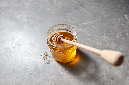 Wooden stick in a glass jar with fresh natural organic honey on a gray concrete background, place for text. Jewish New Year healthy holiday concept.