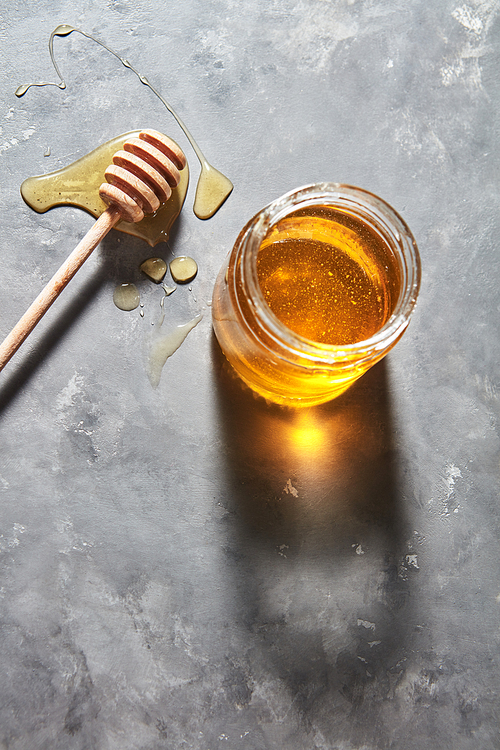 Sweet floral natural honey full a jar and wooden spoon on a gray concrete table, copy space., pure natural sweet goodness. Jewish rosh hashanah holiday concept.