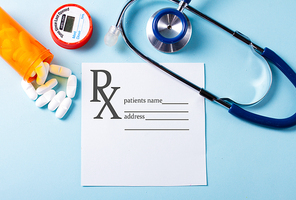 White pills in orange bottle with stethoscope on blue background, prescription and copy space on white paper note