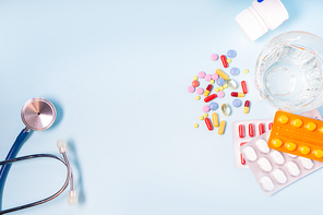 Colorful pills with glass of clear water and stethoscope over blue background with copy space. Medical pharmacy concept
