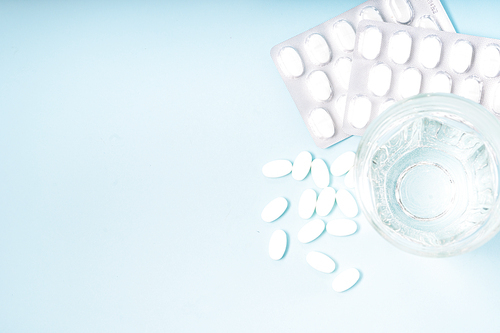 White pills with glass of clear water over blue background with copy space. Medical pharmacy concept