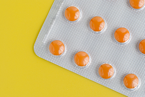 Close-up of a pack of orange pills on yellow background.