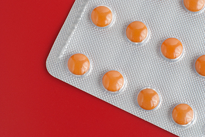 Blister pack of orange pills isolated on red background.
