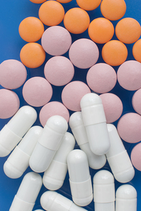 Macro view of white pink and orange pills on blue background.