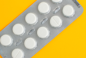 Close-up of a pack of white pills on yellow background.