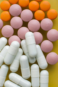 Macro view of white pink and orange pills on yellow background.