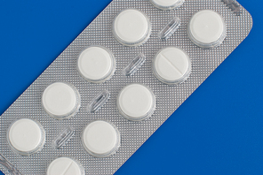 Close-up of a pack of white pills on blue background.