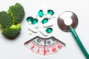 Diet healthy eating weight control and health care concept. Closeup green broccoli stethoscope pills on white scales, choice between