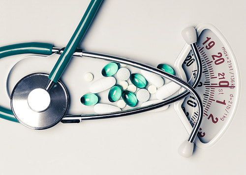 Healthy eating, medicine, health care, food supplements and weight loss concept. Pills with stethoscope on white scales