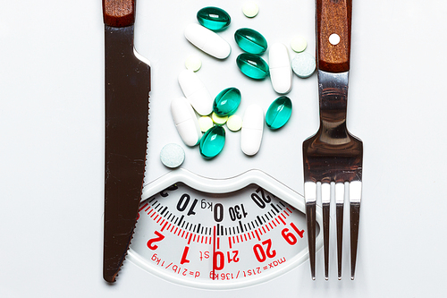 Healthy eating, medicine, health care, food supplements and weight loss concept. Pills with knife fork on dish white scales