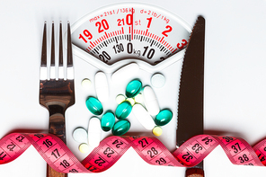 Healthy eating, medicine, health care, food supplements and weight loss concept. Pills with measuring tape on white scales