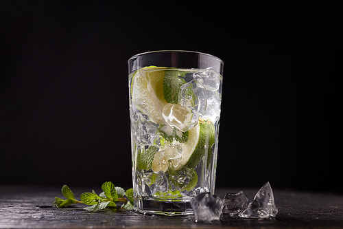 Mojito cocktail with lime, mint and ice cubes on dark background. Traditional summer refreshing drink.