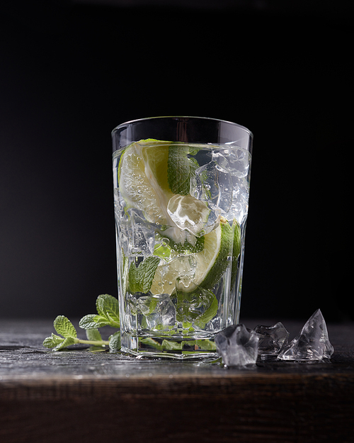 Fresh cold water with lime, mint and ice in a glass on dark stone background