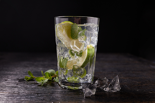 glass of mojito with lime and mint ice cube close-up on dark stone background.