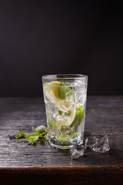 Water Sassi. Vitaminized cleansing water with lemon, mint and ice in a glass on a dark background. The concept of dietary and vegetarian nutrition.