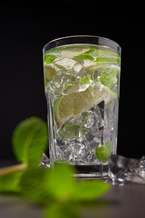 Cold and refreshing infused detox water with lime, ice and mint in a glass on dark background. The concept of dietary and vegetarian nutrition.