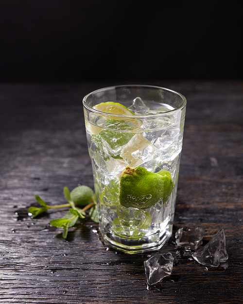 Glass of iced Mojito and ingredients- slice lime, ice and mint leaves isolated on black, cold drink in summer