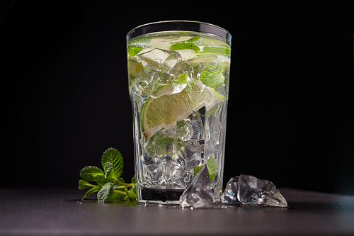 Cold lemonade with lime, mint and ice in a glass on stone background. The concept of dietary and vegetarian nutrition.