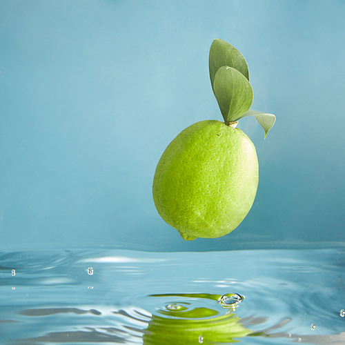Beautiful green limes sinking into water on blue background