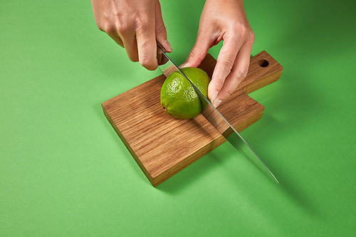 Citrus organic fruits. Female hands cut a juicy green ripe lime to slices for making homemade natural lemonade. Concept of healthy food and drink.