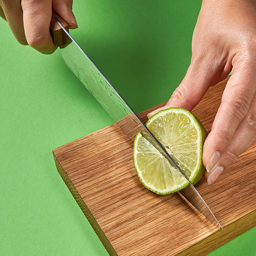 female hands cutting organic green ripe lime with steel knife for preparation detox baverage for ary healthy food. concept healthy food.