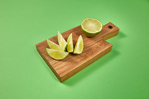 Healthy food concept. Natural organic citrus fruit - slices of of green organic lime on a wooden board on green with copy space .