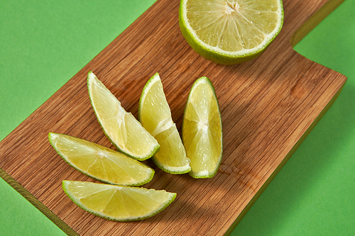 Juicy slices and half of ripe green lime on a wooden board on a green background. Healthy food concept.