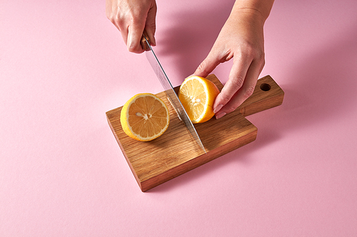 Citrus fruits on brown board cutting by female hands. Top view of citrus fruit - slices of of yellow organic lemon on a wooden board on a pink. Healthy food concept.
