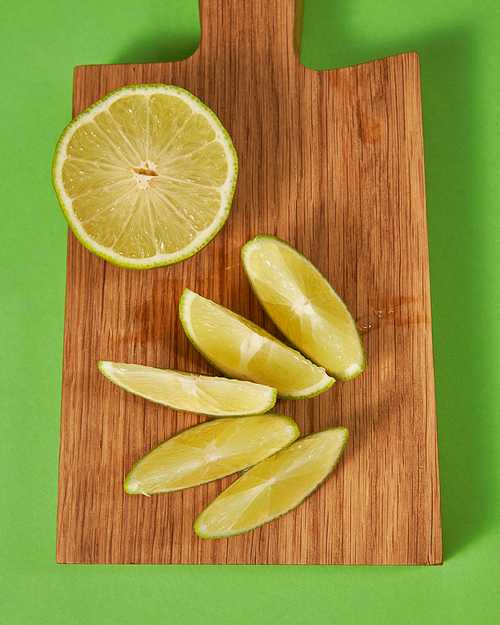 Top view of citrus fruit green lime on a wooden brown board on a green. Half and slices of natural organic fruit on cutting board.