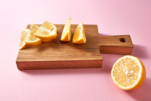 Juicy slices and half of ripe yellow lemon on a wooden brown board on a pink . Healthy food concept.