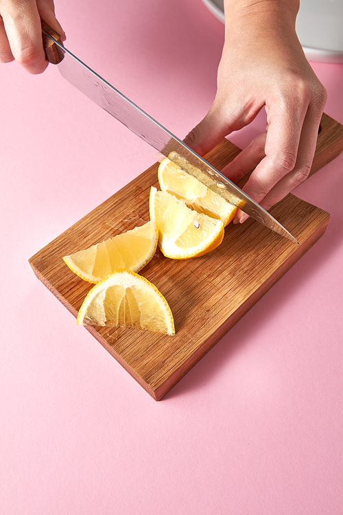 Slices of yellow lemon on a wooden board on a green. Female hands cutting a ripe lemon for preparing homemade fresh cocktail on pink background. Healthy food concept.