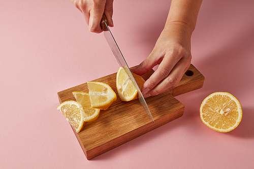 Woman cutting organic yellow ripe lemon with steel knife on pink for preparation detox drink for dietary healthy food. Concept vegetarian food.