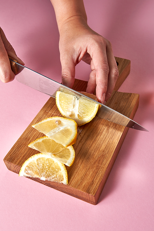 Citrus slices of yellow organic lemon on a wooden board on pink. Natural citrus fruits on brown board cutting by female hands. Healthy food concept.