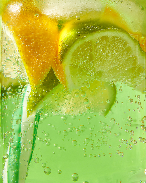 a natural fruit background with macro lime slices, lemon and a colored  plastic straw in a glass jar with aerated gassed bubbles. concept of cold alcoholic or non-alcoholic summer drinks.