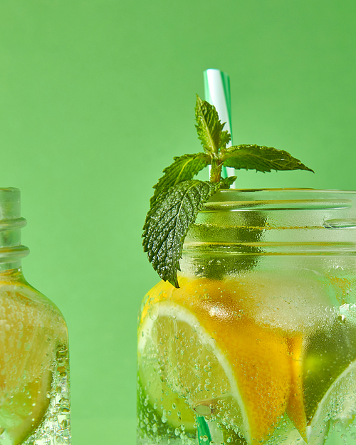 A close-up of a sprig of green mint in focus in a glass jar with cold natural handmade lemonade on green background. Concept of cold alcoholic or non-alcoholic summer drinks.