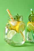Two glass jars with homemade sparkling cocktail with aerated gassed bubbles, natural ingredients,ice and plastic straws on green background.