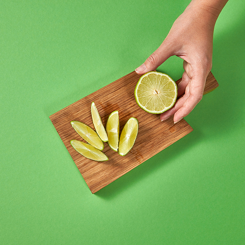 Natural organic fresh lime slices on a wooden board with copy space. Female hands hold a piece of lime. The concept of healthy natural vegetarian food.