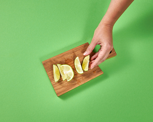 Organic natural fresh lime slices on a wooden board. Female hands takes a piece of lime for preparing homemade natural lemonade. Concept of healthy natural vegetarian food.