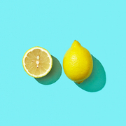 Half and whole a juicy lemon on a blue background with shadow and copy space. Ingredient for drink. Top view