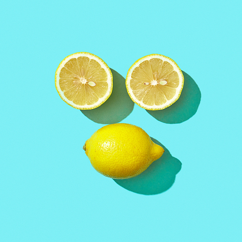 Yellow lemon and halves in the form of faces presented on a blue background with shadows and space for text. Flat lay