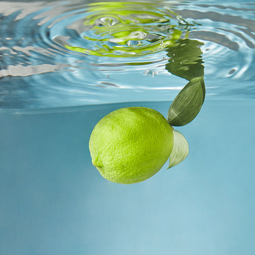Yellow fresh lemon with green leaves whole under water on a blue background