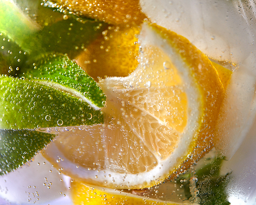 Slices of lemon and lime with bubbles of water in a glass. Macro photo of refreshing lemonade