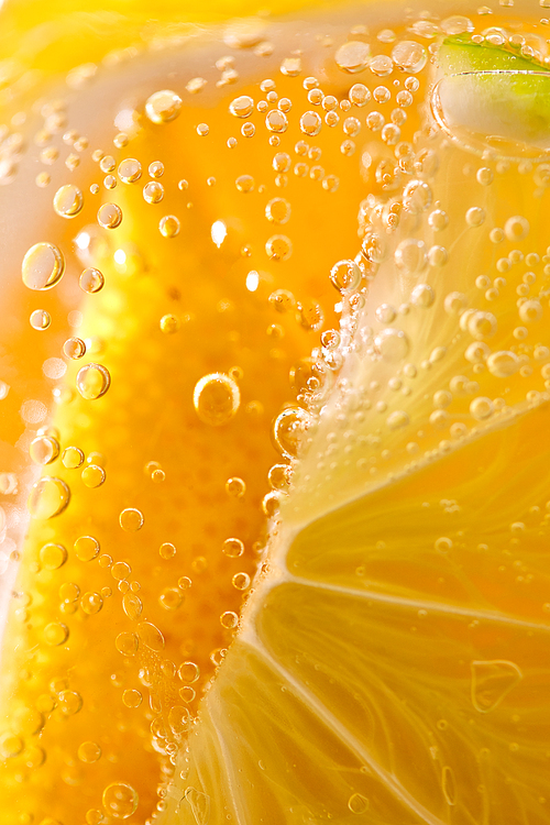 Juicy slices of ripe lemon with bubbles in a glass of water. Macro photo of refreshing lemonade