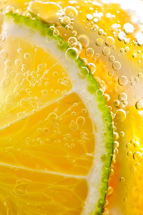 Macro photo of yellow lemon slices and lime with lots of bubbles in a glass with water. Summer refreshing cocktail