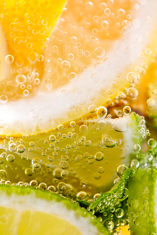 Ripe sliced pieces of lemon and lime in a glass with water and bubbles. Macro photo of summer beverage